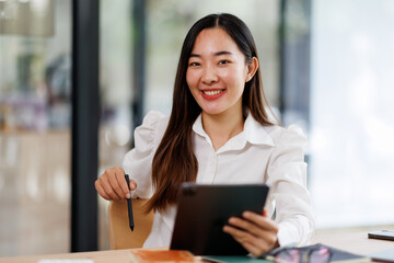 Obraz premium Young fun smiling asian successful employee business woman work use hold tablet pc computer stand at workplace white desk modern office. Achievement career concept 