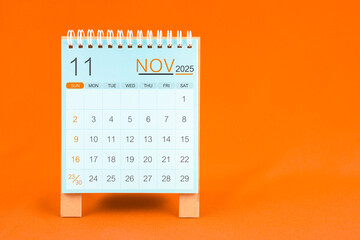 November 2025 desk calendar stand on orange textile background.