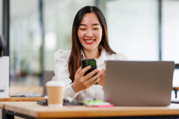 Obraz premium Portrait of a happy Asian businesswoman using phone and work on laptop, Asian businesswoman working in modern office. 