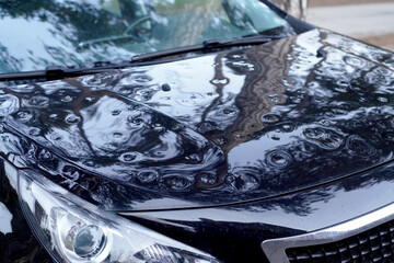Close-up view of the hood, front pillar, and part of the roof of a car heavily damaged by hail....