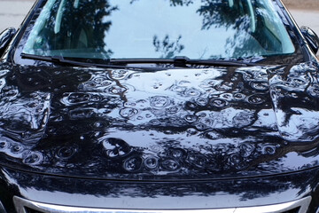 Close-up of a car hood with numerous dents caused by hail or falling debris. The reflective surface...