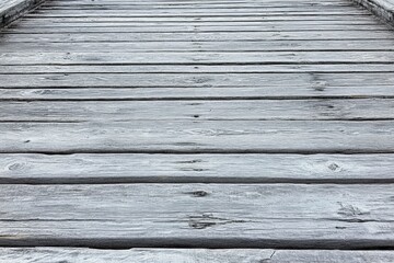 Obraz premium Weathered grey wooden planks forming a walkway, showing texture and age. The perspective is from a low angle, emphasizing the lines of the wood.