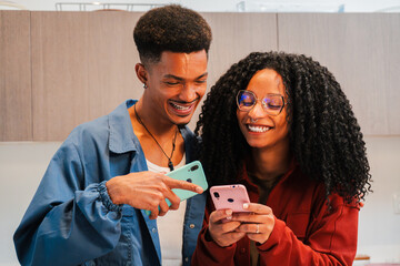 Happy couple enjoying a delightful moment together while interacting with their smartphones and sharing laughter over a fun application on their mobile devices in a cozy indoor atmosphere