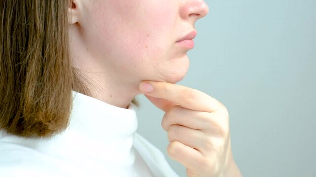 Female face with double chin close-up on gray background, side view.