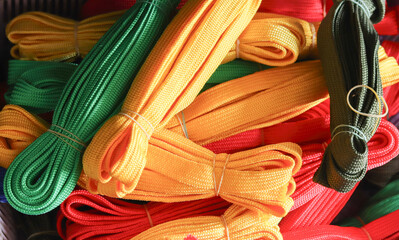 A colorful assortment of bundled nylon ropes in various hues, piled together with a mix of vibrant greens, yellows, reds, and browns. Represents crafting supplies, textile textures, and a spectrum of 