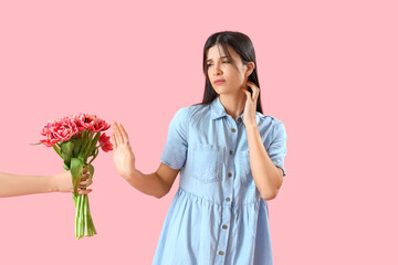 Allergic young woman rejecting tulips on pink background