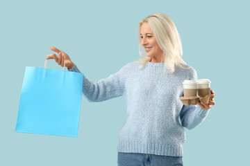Mature woman with takeaway cups of coffee and shopping bag on blue background