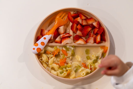Child enjoying colorful fruit and pasta on a plate during meal time