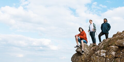 Three people on a rocky cliff, enjoying the view. Outdoor adventure, friends on a cliff, enjoying nature. Cliff, friends, adventure, nature, outdoors. Friends on hiking adventure in nature.