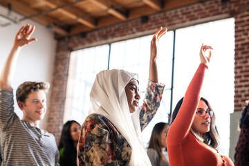 Woman in hijab and diverse group of people raising hands in a Seminar room setting, showing...