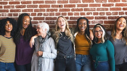 Diverse group of women smiling and standing together against a brick wall. They appear happy and connected, showcasing friendship and diversity. Diverse group of women united, standing together.