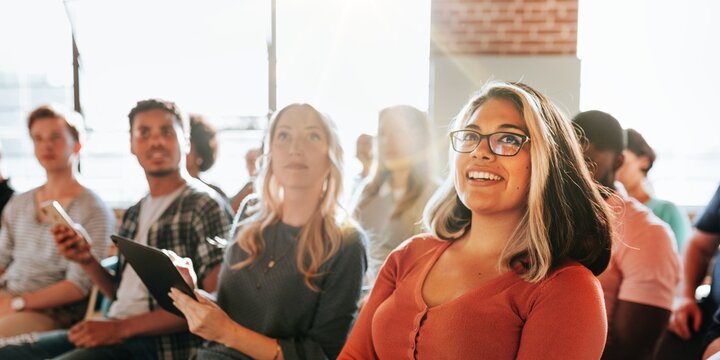 Diverse group of people, including a smiling woman, attending seminar. The seminar audience includes men and women of various ethnicities, all engaged in the seminar. Community seminar with audience.