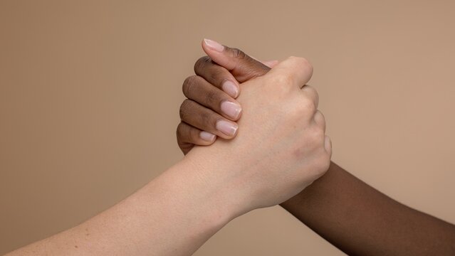 Close-up of two diverse hands clasped together. Hands in unity, symbolizing friendship and support. Hands in a gesture of togetherness.Multi ethnic people togetherness and support, two hands clasping