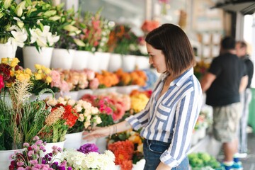 Woman browsing colorful flowers at a market. Flowers in various shades. Market filled with vibrant flowers. Woman enjoying the flower market scene. Woman shopping at market.