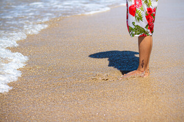 Legs of Asian adult woman with temporary tattoo in floral beach dress standing barefeet on beach sand in sunny day during summer holiday