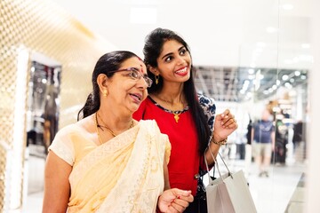 Two Indian women shopping, smiling, holding bags. They enjoy shopping together. Bright store, happy Indian women, shopping bags, joyful expressions, retail therapy. Happy Indian women enjoy shopping.