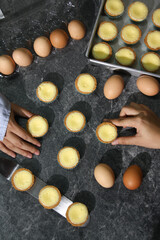 Two hands are arranging small egg tarts and several raw eggs