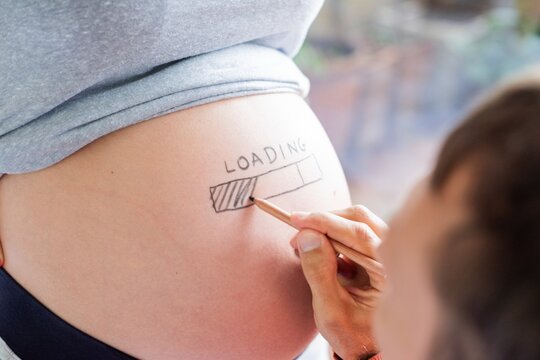 Close-up of a pregnant belly with a loading bar drawn on it. A hand colors the bar, symbolizing pregnancy progress. Creative pregnancy concept. Woman pregnancy, expecting baby concept.