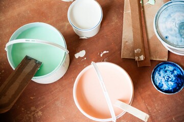Buckets of colorful paint on a wooden surface. Green paint, pink paint, and blue paint in containers. Paint supplies for creative projects. Color paint buckets in construction site.