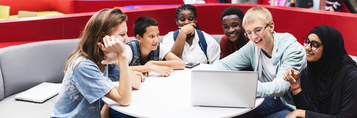 Diverse group of students collaborating around a laptop. Young people, teamwork, and learning. Engaged students sharing ideas in a modern setting. Diverse students in school discussion.