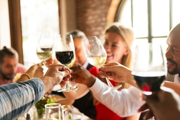 Group of diverse people clinking wine glasses celebrate toast at a social gathering. Diverse people enjoying wine, laughter, and celebration in cozy restaurant. Diverse people toast wine to celebrate