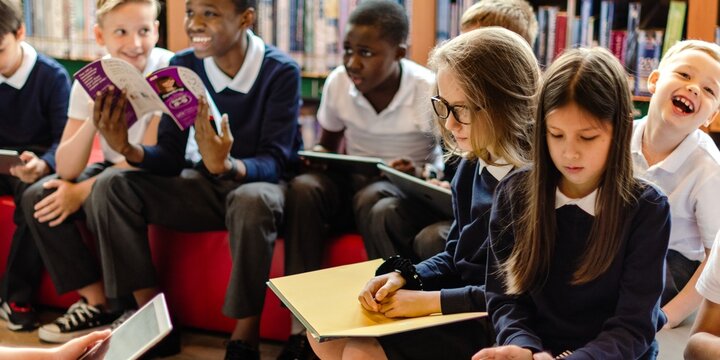 Group of diverse children in school uniforms reading and writing in a library. Kids engaged in learning, sharing books, and enjoying study time together. Diverse people in library. - Powered by Adobe