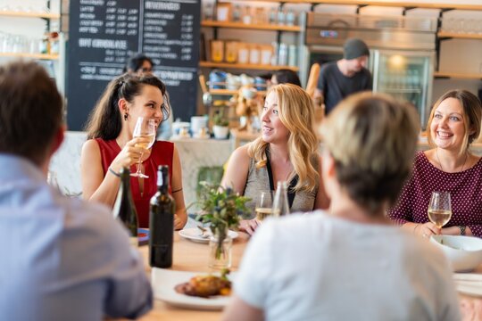 Group of diverse people enjoying wine at a cozy cafe. Smiling friends, casual and relaxed atmosphere. Social gathering with drinks and laughter. Diverse friends enjoy wine and chatting at cafe