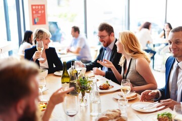 Group of professional people dining at a restaurant, enjoying food and wine. Lively conversation and laughter. Dining atmosphere with diverse group of friends. Professional people at business lunch