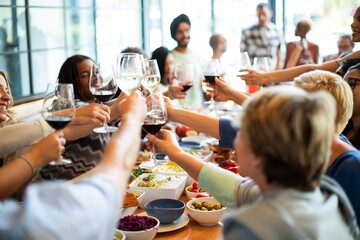 Group of people toasting with wine glasses at a gathering. Diverse group enjoying a meal, celebrating together with food and drinks in a cheerful setting. Happy people wining and dining at restaurant.