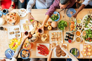 Top view of a diverse group enjoying a meal. People share food, toast drinks, and celebrate. A variety of dishes and drinks on a wooden table. Buffet table with delicious food photo from top view.