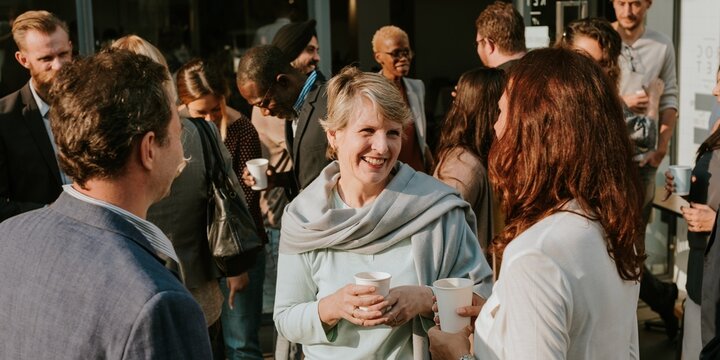 Group of diverse business people socializing outdoors, holding cups, smiling, and chatting. Casual gathering enjoying conversation and drinks. Diverse businesss people mingle in social event outdoors.