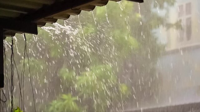 Heavy rain pouring from a roof's edge, blurring the green foliage in the background, creating a tranquil and serene atmosphere