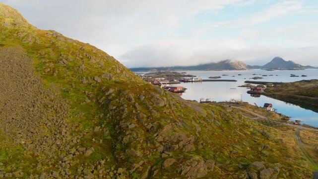 Ballstad village in Lofoten, Norway, with rolling green hills and the ocean stretching to the horizon, aerial dolly reveal over hillside
