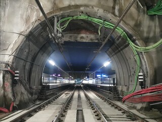 Illuminated metro tunnel leading to a station platform. Visible tracks, catenary, cables, and...