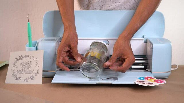 Hands working with vinyl cutter in design studio, decorating jar with colorful sticker