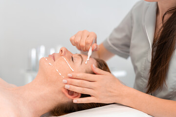 Dermatologist applying cream on the face of a woman lying on bed. Young lady receiving a skincare procedure in a beauty salon, enjoying a relaxing treatment