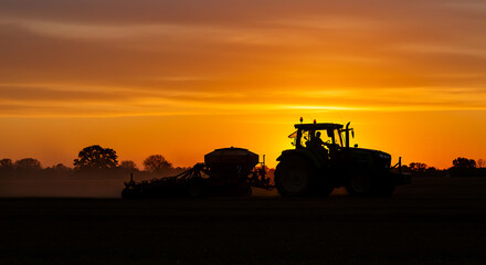 Fototapeta premium Silhouette of a Tractor Working at Sunset Golden Hour Farming Agriculture Scene
