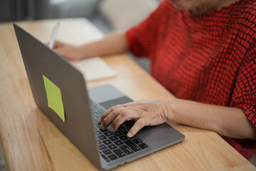 Senior woman using laptop while taking notes in living room, showcasing technology and modern lifestyle, promoting creativity and productivity at home