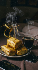 A steaming cup of warm coffee next to ready-to-serve Ketupat on a plate, depicts a comfortable and peaceful atmosphere, perfect for relaxing moments.