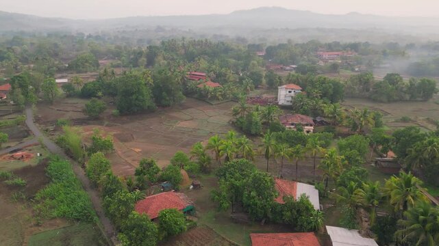 A stunning drone shot of Avalegaon, Kudal village in Konkan, Maharashtra, India showcasing a serene traditional houses, lush green trees, vast fields and majestic mountains under a clear pink sky