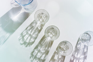 Water Glasses and water jug with Shadows and sunlight Reflection on white background, colored photo...