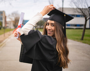 Happy graduate latin student woman holding diploma and adjusting graduation cap