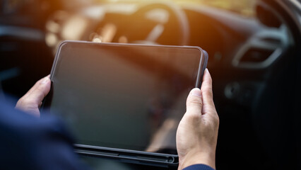 A person is holding a tablet in their hand, possibly using it to navigate a car. Concept of technology and modernity, as well as the idea of being in control of a vehicle