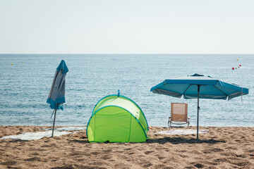 Equipement de plage pour un vacancier. Parasol, tente et chaise sur une plage de sable fin devant...