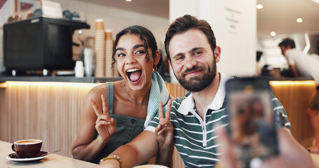 Photography, excited and couple in cafe on date with memory, bonding or social media post. Peace sign, happy and man with woman in coffee shop for profile picture in morning at restaurant together