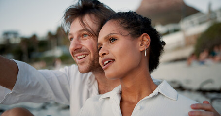 Conversation, couple and relax with hug on beach, vacation holiday and bonding together for anniversary. Pointing, man and woman in interracial relationship for love embrace, travel or smile on ocean