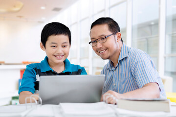 Asian teacher helping his student to use a laptop