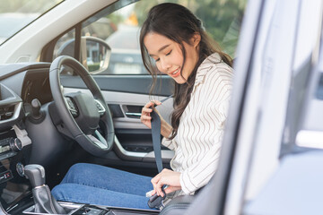 Happy smile brunette asian young woman hand fastens a seat belt sitting in front of car before...
