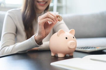 Saving money wealth concept, asian young business woman hand putting coin into piggy for saving...