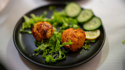 Delicious indian tikka chicken with salad and cucumber on black plate